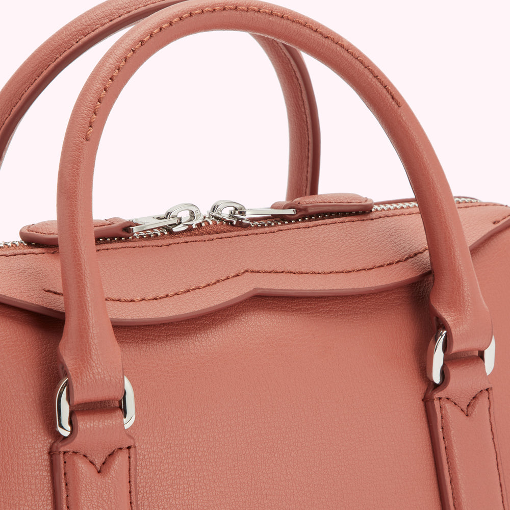 Close-up of a dusty rose-coloured leather handbag with silver hardware.

