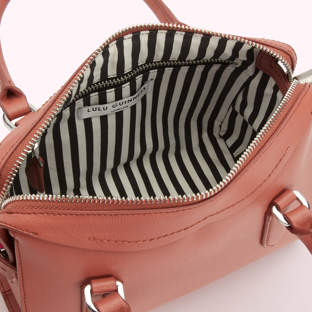Dusty rose Lulu Guinness satchel bag open to reveal a black and white striped interior.
