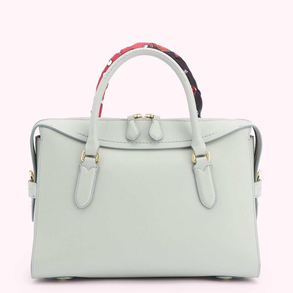Light green leather handbag with gold hardware and a patterned scarf detail on the handle.
