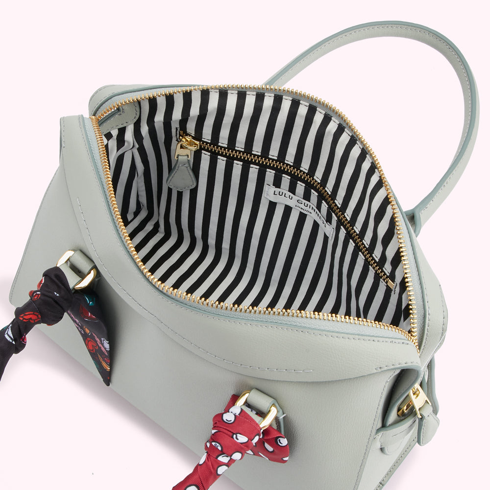 Sage green Lulu Guinness satchel with black and white striped interior and red and black silk scarves attached to the handles.
