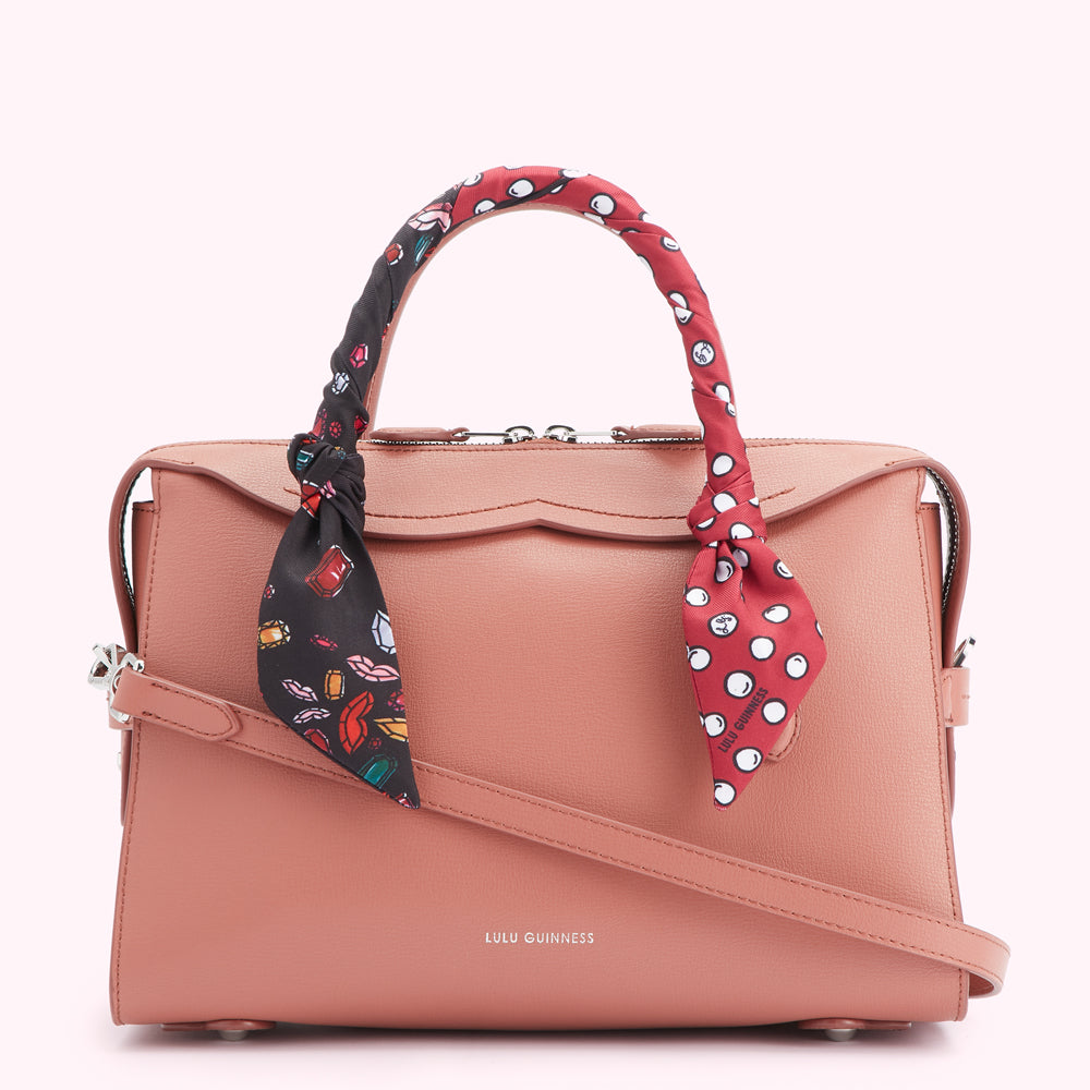 Dusty rose Lulu Guinness satchel bag with a patterned scarf wrapped around the handle.