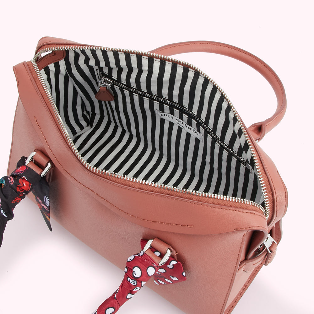 Dusty rose Lulu Guinness handbag open to reveal black and white striped interior lining and attached silk scarves.