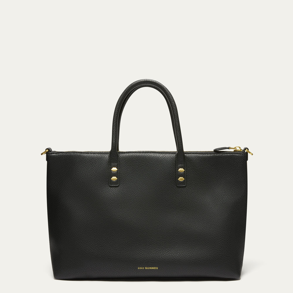A black pebbled leather tote bag with double top handles, gold-tone hardware, and a small gold 'LULU GUINNESS' logo on the bottom front, shown against a light off-white background.