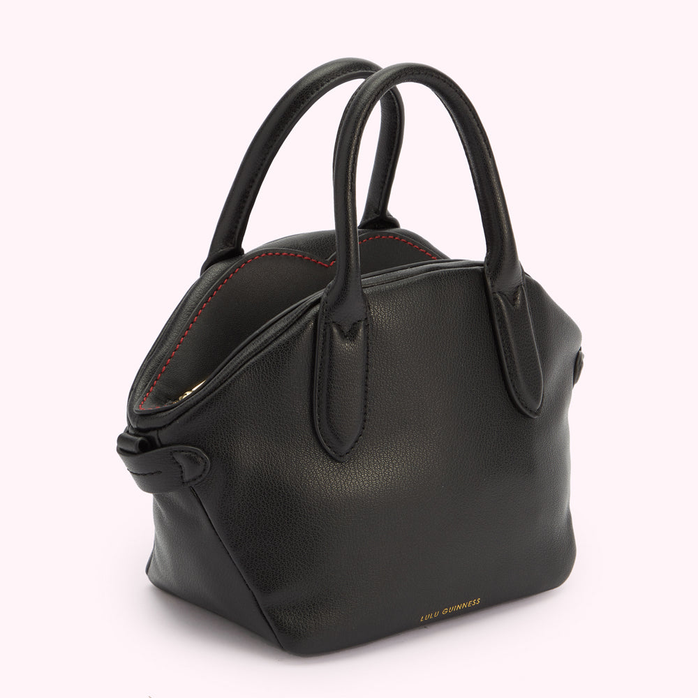 An angled side image of a black leather handbag with a top handle and a gold foil Lulu Guinness logo. Revealing contrasting red stitching on the top.