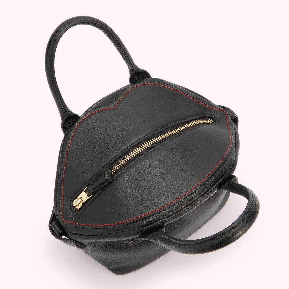 A above image of the top of a black leather handbag showing the gold zip fastening and lip shaped contrasting red stitching.
