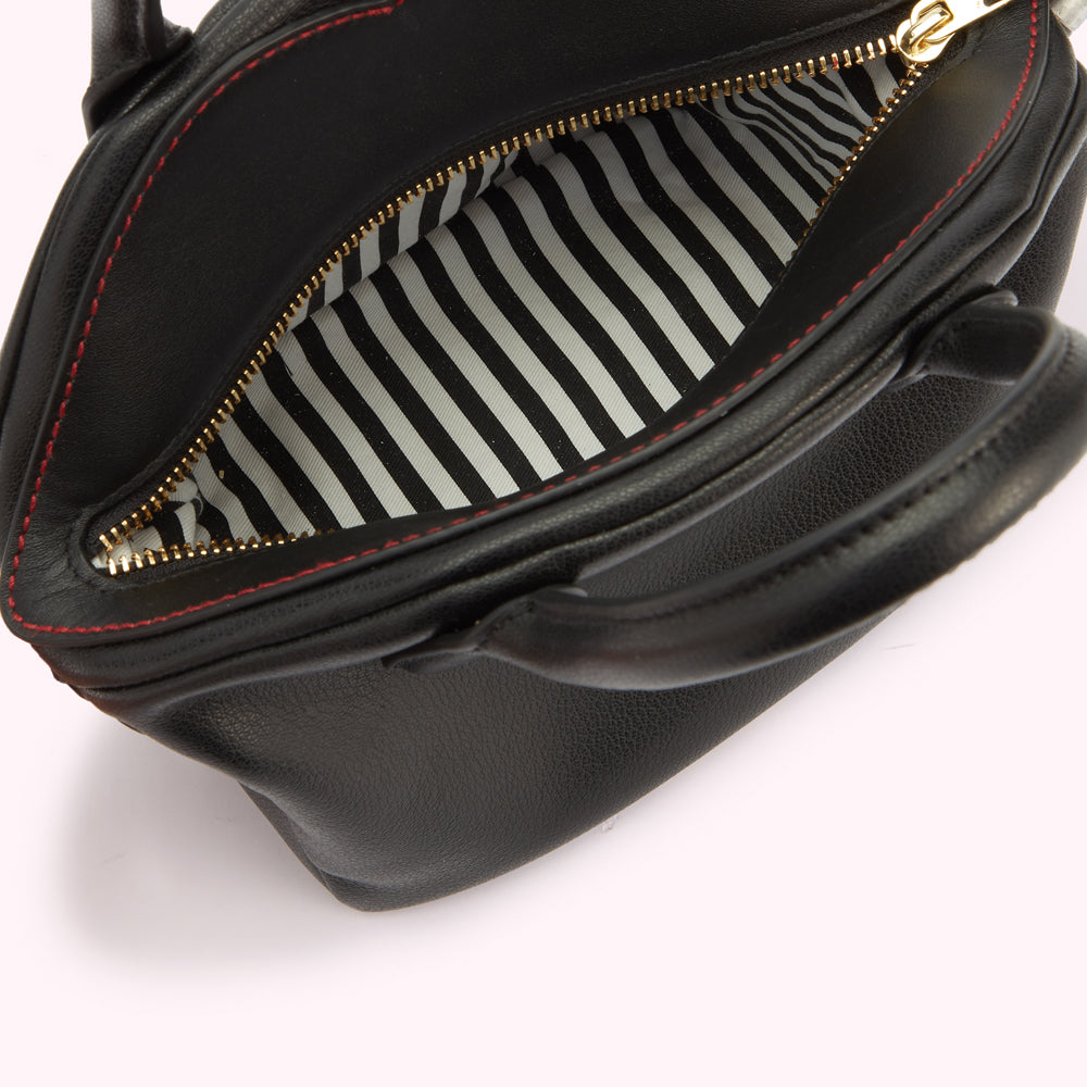A close-up image of a black leather handbag open revealing the white and black striped lining and contrasting red stitching across the top.