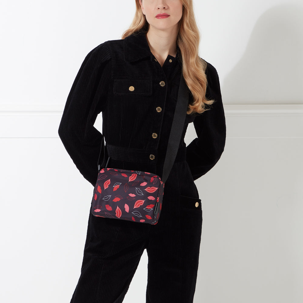 Woman in black corduroy jumpsuit with black crossbody bag featuring a red lips print.