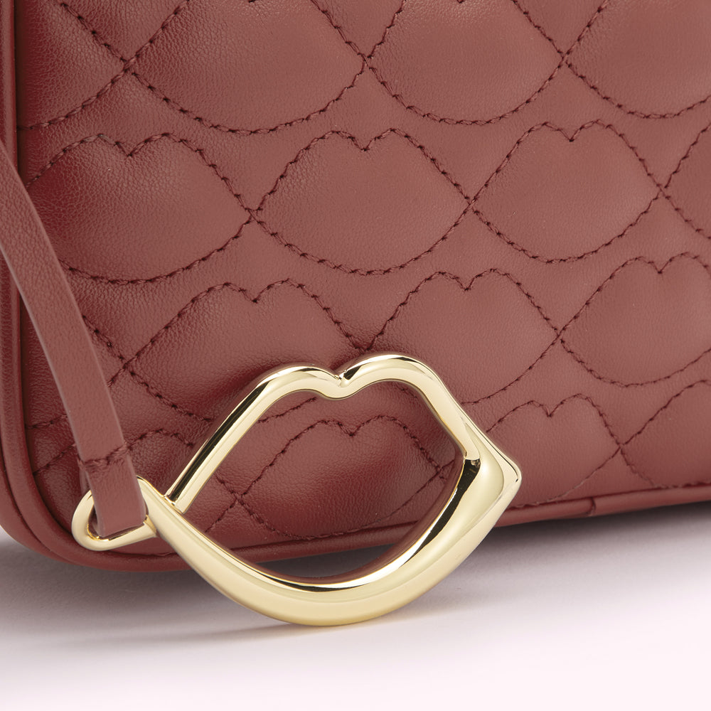 Close-up of a burgundy quilted leather bag with a gold lip-shaped detail.
