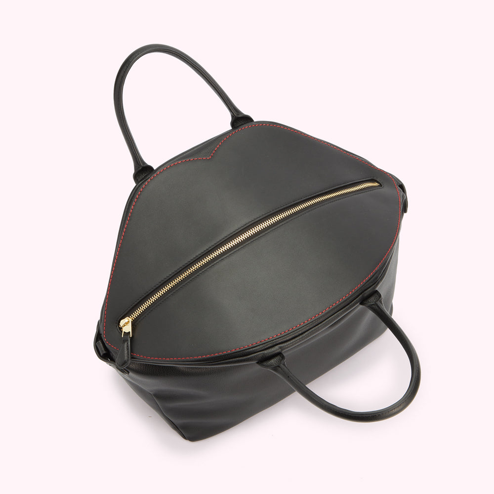 A above image of the top of a black leather tote bag showing the gold zip fastening and lip shaped contrasting red stitching.