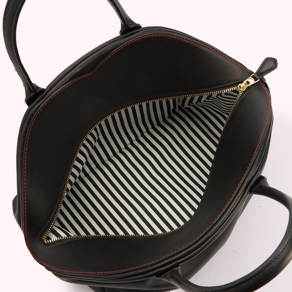 A close-up image of a black leather tote bag open to reveal the white and black striped lining and contrasting red stitching across the top.