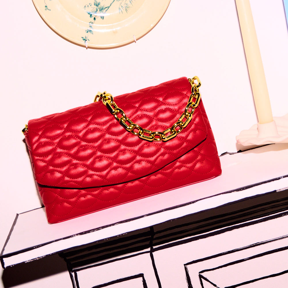 Red leather quilted clutch bag with a gold chain sitting on a mantel piece. 