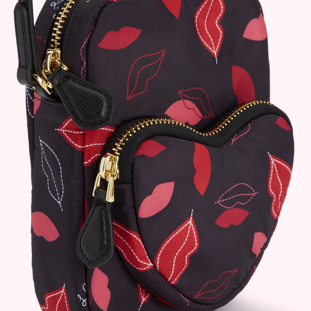 Close-up of a black heart-shaped bag with a red lips print and gold zippers.

