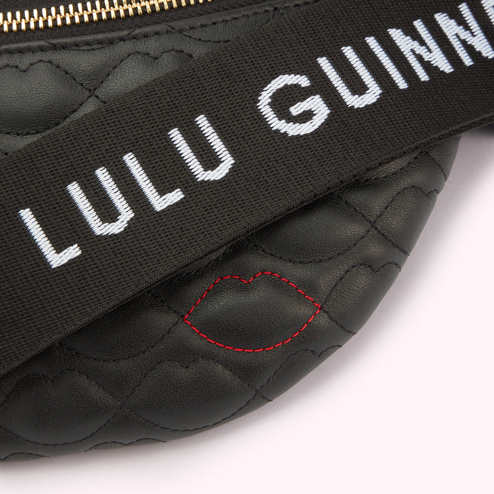 A close-up detail image of the lip shaped quilting, red lip stitching and branded 'Lulu Guinness strap on a black leather belt bag.