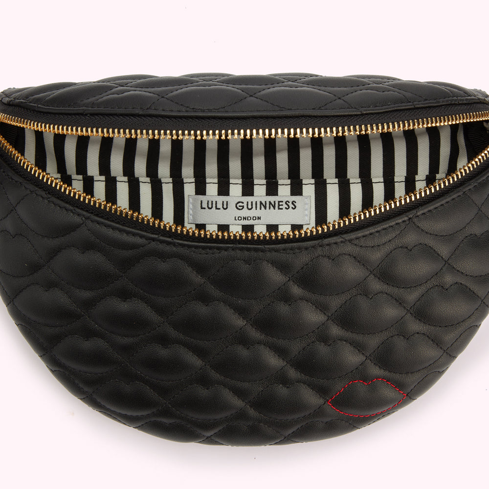 A detail image of a black leather belt bag with lip shaped quilting, gold zip and a contrasting red stitched lip on the bottom edge open revealing the black and white striped lining.