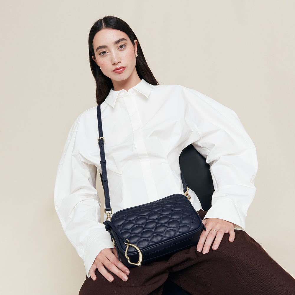 Woman holding a navy blue leather quilted handbag against a beige background