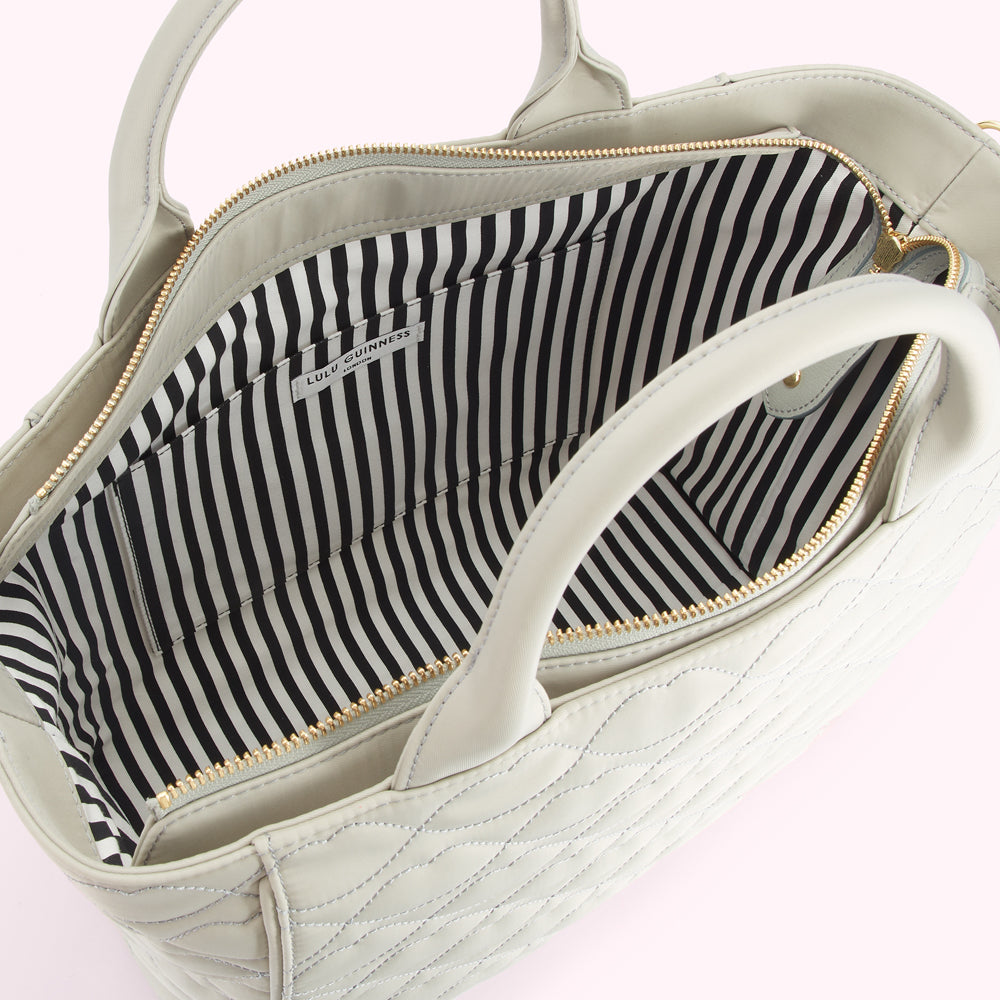 Interior of a light beige quilted Lulu Guinness handbag with a black and white striped lining.
