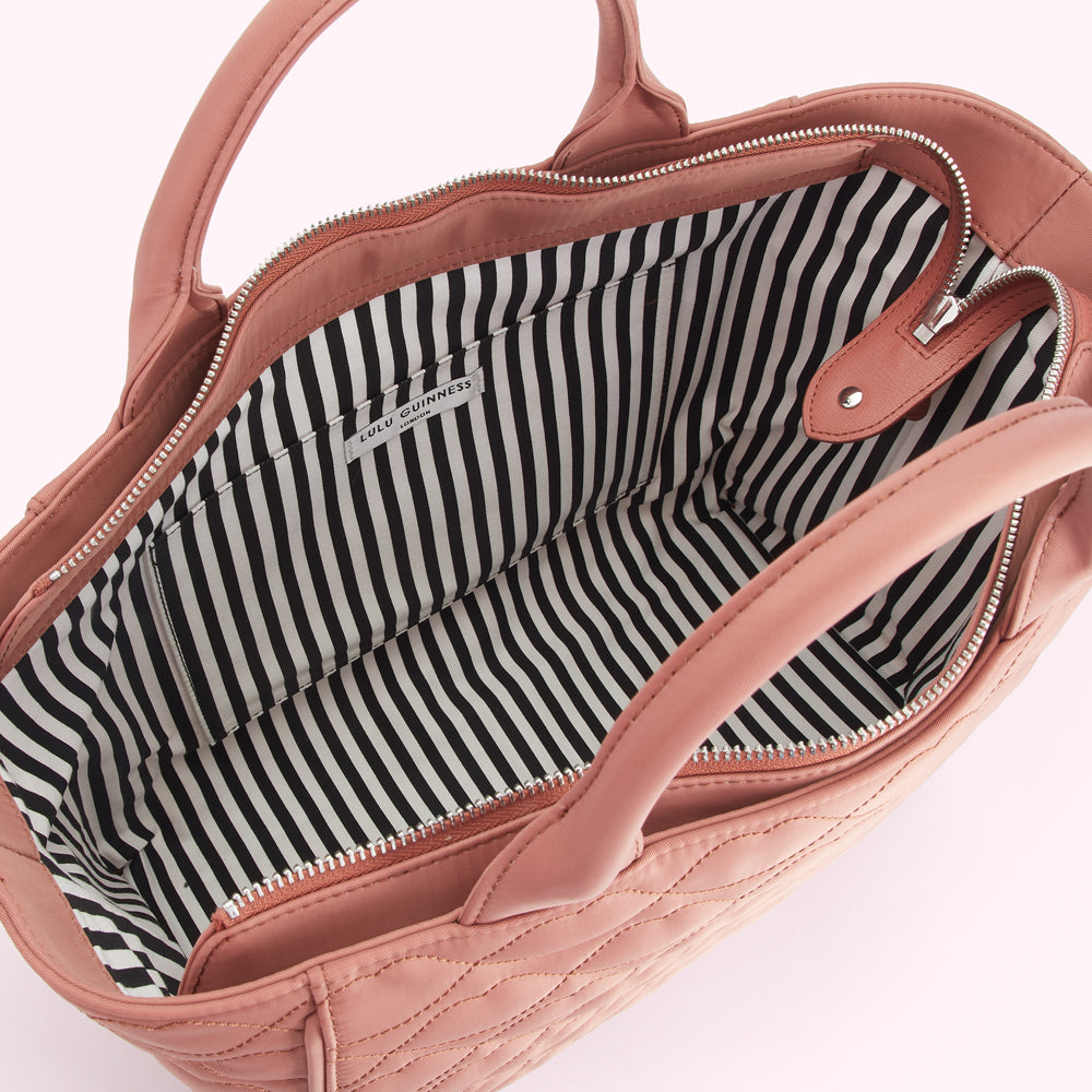 Inside of a dusty rose Lulu Guinness quilted tote bag showing the black and white striped lining.