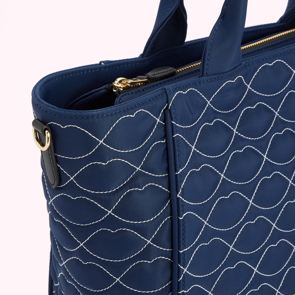 Close-up of a navy blue quilted tote bag with a lip-shaped pattern stitched in white.
