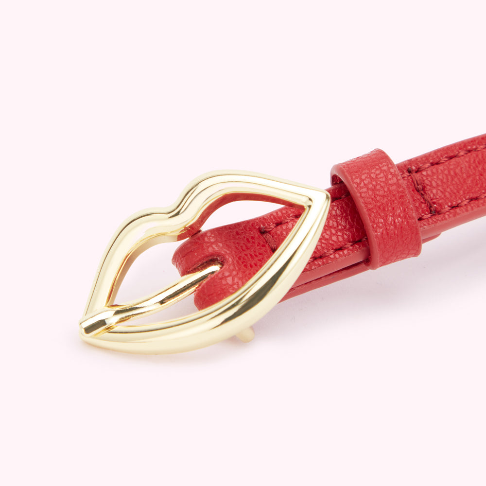 Close up image of a gold lip shaped buckle on a red leather belt.