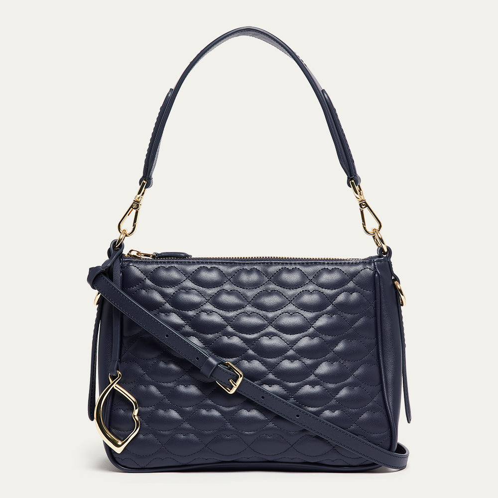 Navy leather quilted handbag with gold lip charm on a light gray background