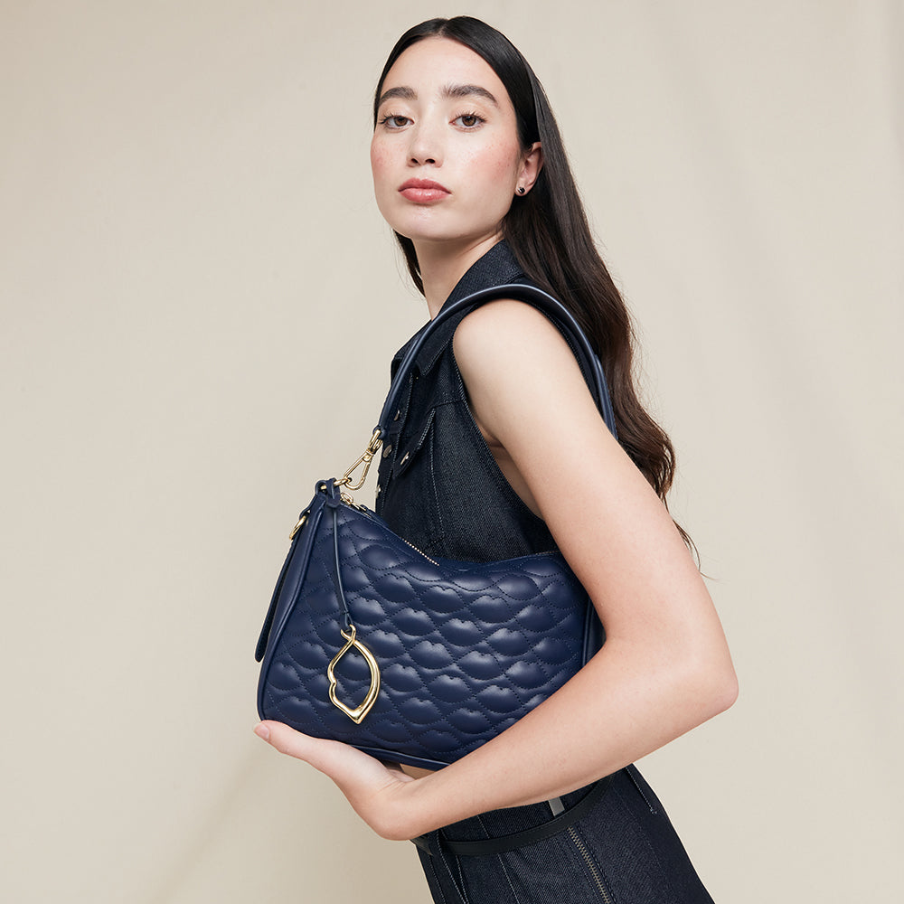 Woman holding a navy blue leather quilted shoulder bag with a gold lip charm against a beige background