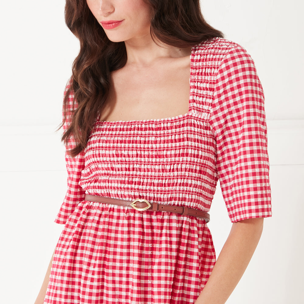 Close up image of a women wearing a red gingham print dress and a tan brown leather belt with a gold lip buckle on her waist.