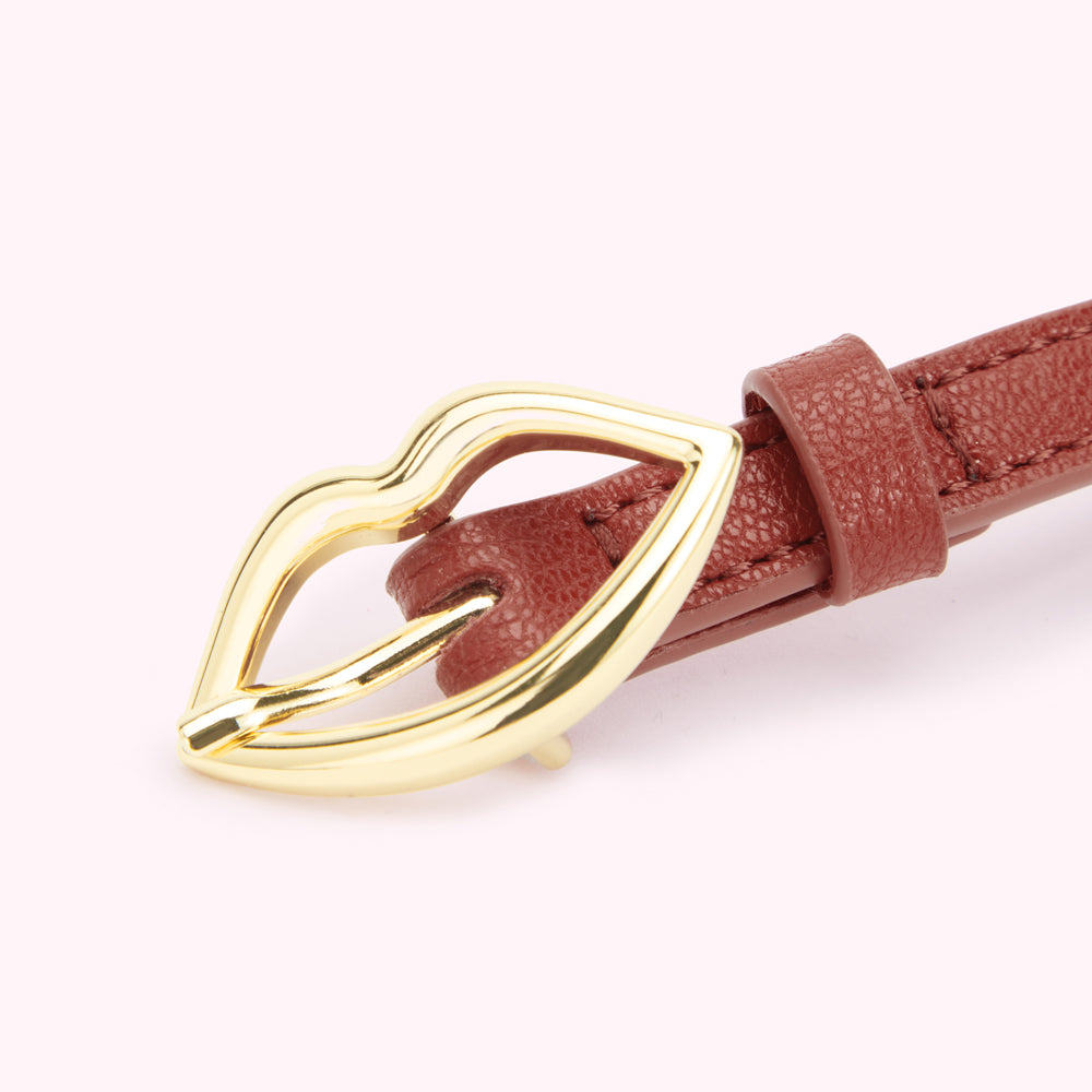 Close up image of a gold lip shaped buckle on a tan brown leather belt.