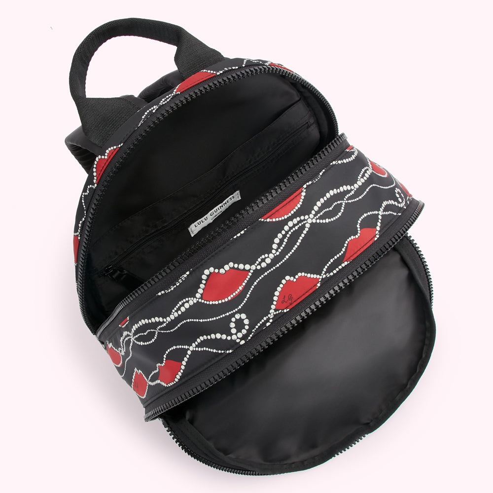 Open black Lulu Guinness backpack with red lips and pearls print.