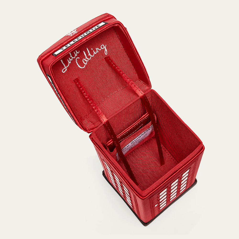 Close up of the inside of a red phone box shaped handbag with 'Lulu Calling' embroidery on a light gray background