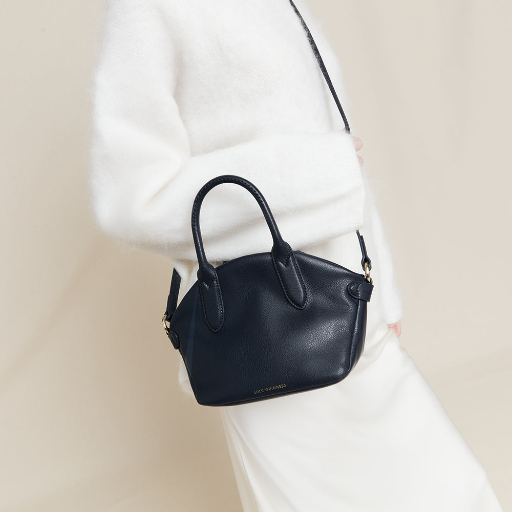 Navy blue leather handbag held by a person wearing a white outfit against a beige background