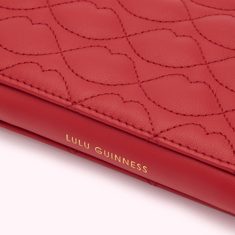 Close-up of a red Lulu Guinness quilted leather item with the brand name embossed in gold.
