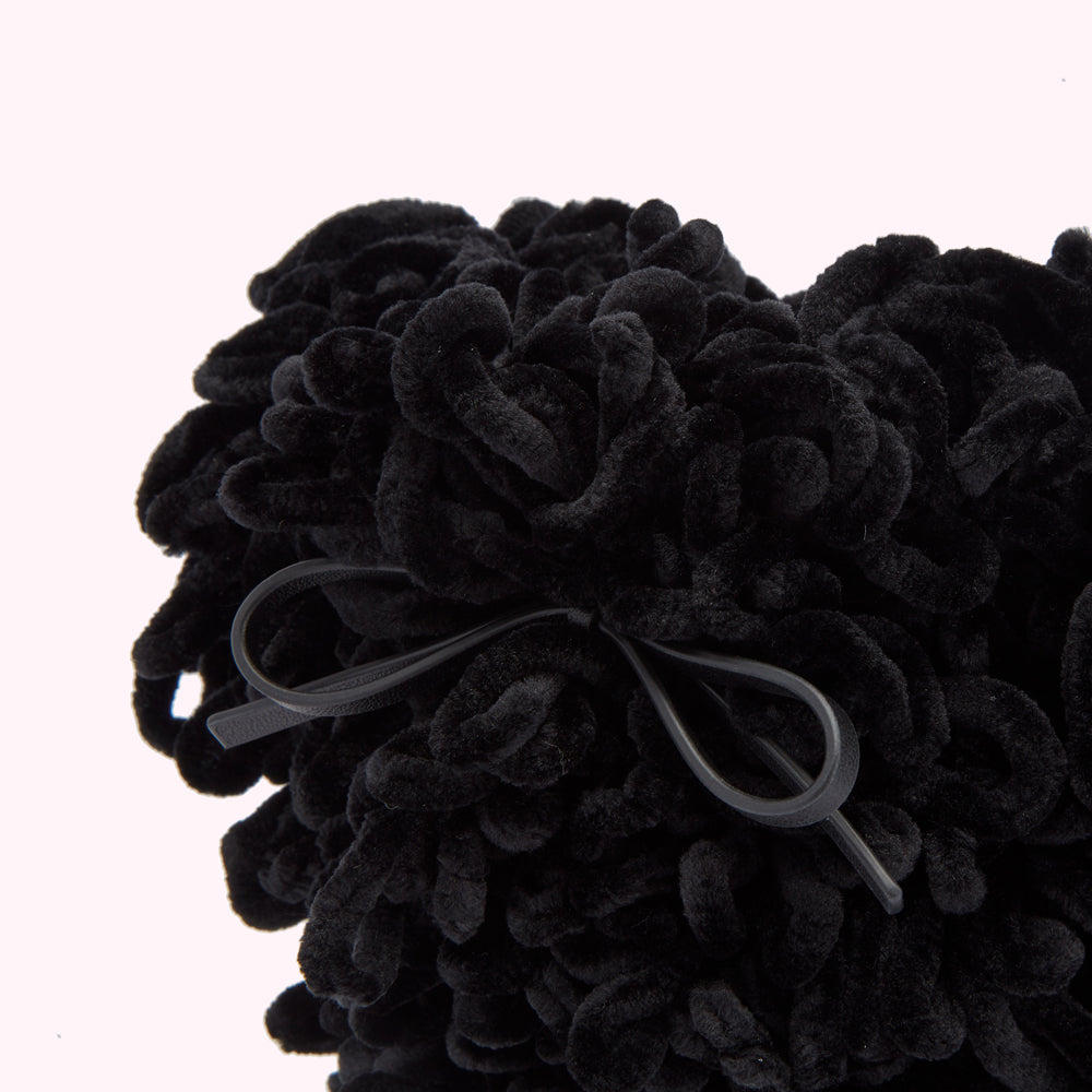 Close-up of a black, fluffy dog-shaped bag with a black leather bow.