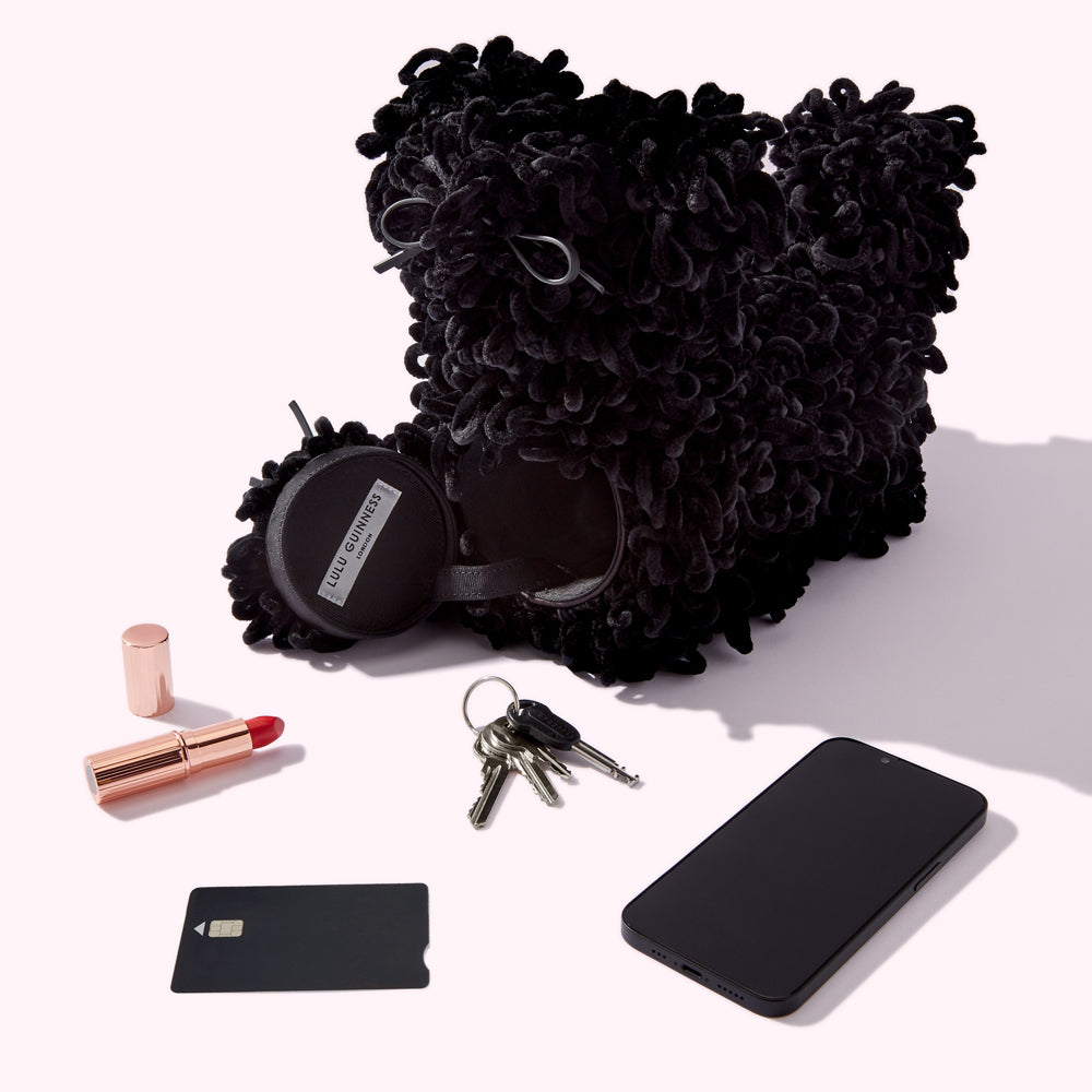 Black fluffy dog-shaped bag with a lipstick, keys, credit card, and smartphone on a white background.