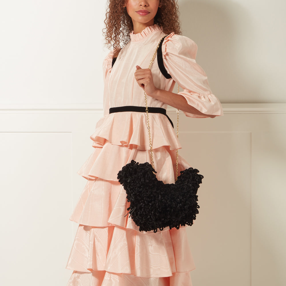 Woman in peach dress holding black fluffy handbag with gold chain strap.
