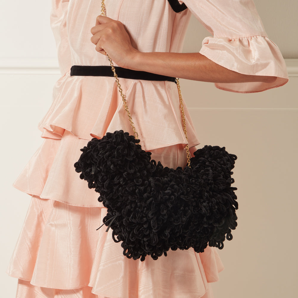 A woman in a peach dress holds a black, fluffy handbag with a gold chain strap.