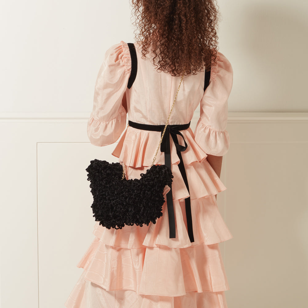 Woman from behind wearing a peach tiered dress and carrying a black fluffy handbag with a gold chain strap.