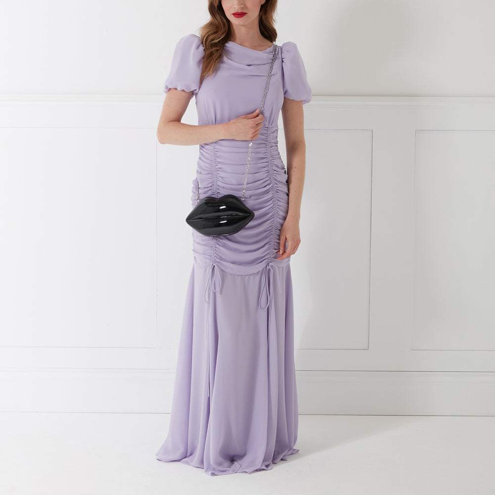 Woman in lavender dress holding black lip-shaped purse.
