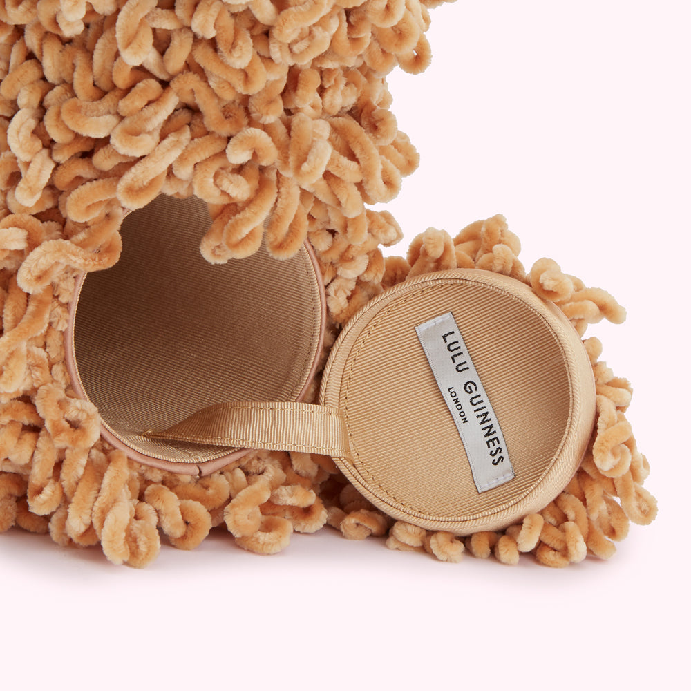 Close-up of a beige Lulu Guinness cylindrical bag with a fluffy, textured exterior. The bag is open, revealing a beige satin lining and a small, removable circular interior case with the brand label visible.