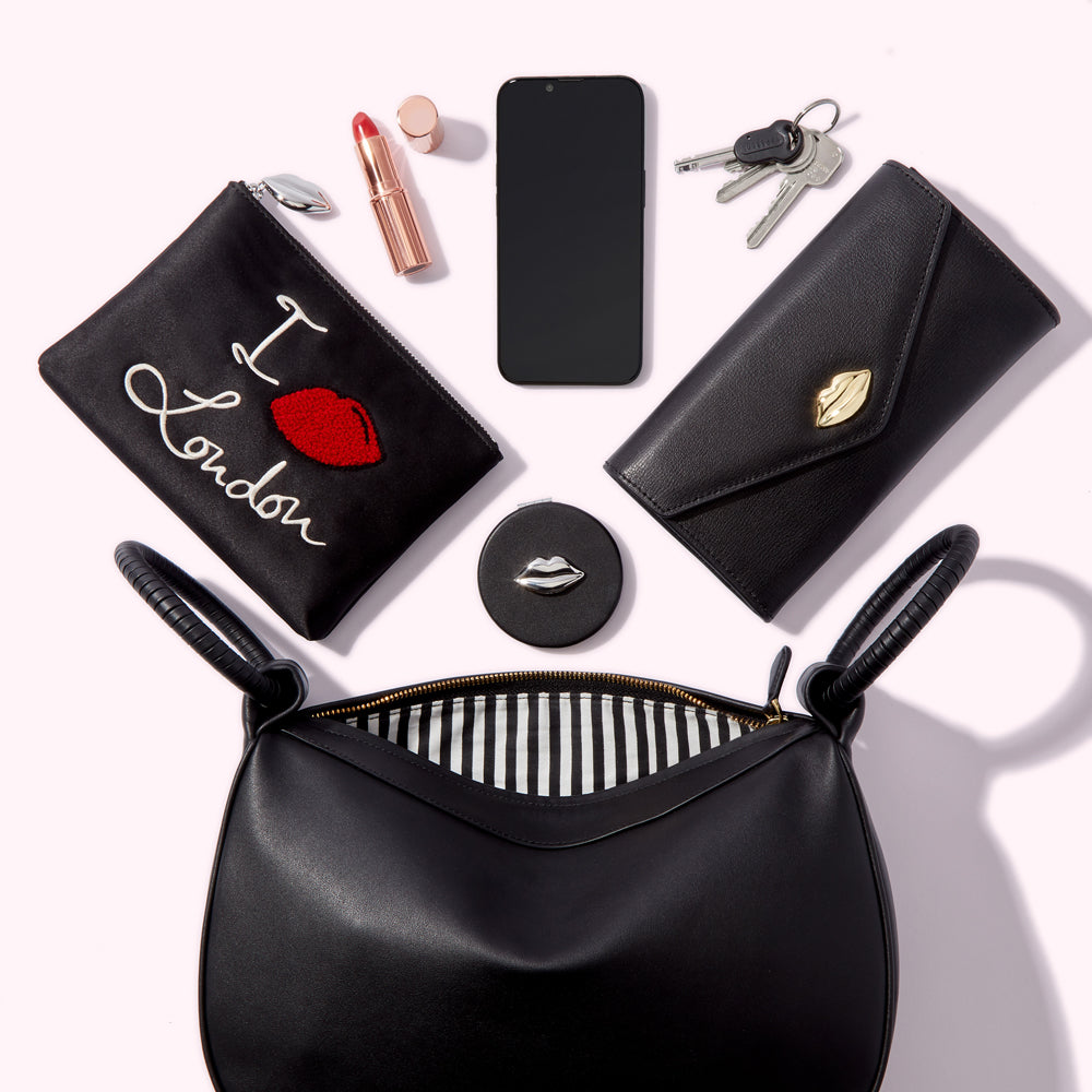 Flat lay of a black handbag, purse, compact mirror, lipstick, phone, and keys against a white background.