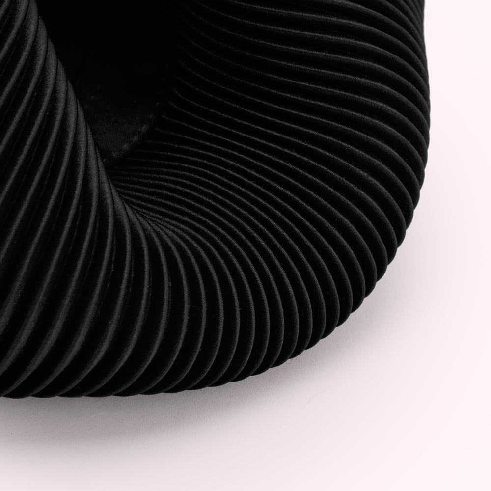Close-up of a black, pleated fabric with a curved form against a white background.
