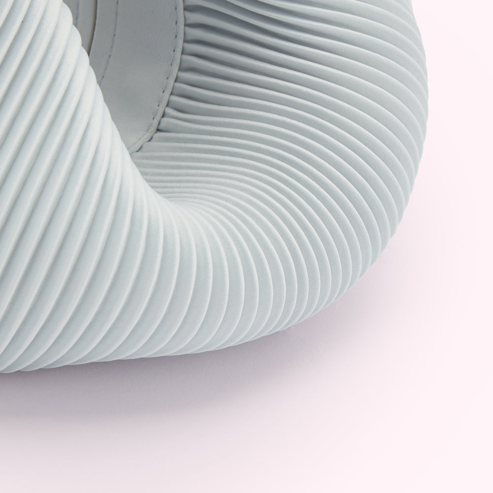 Close-up of a light grey pleated fabric forming a curved shape against a white background.
