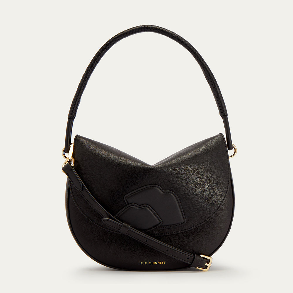 Black leather handbag with gold accents, shoulder strap and lip detail on the front on a light gray background