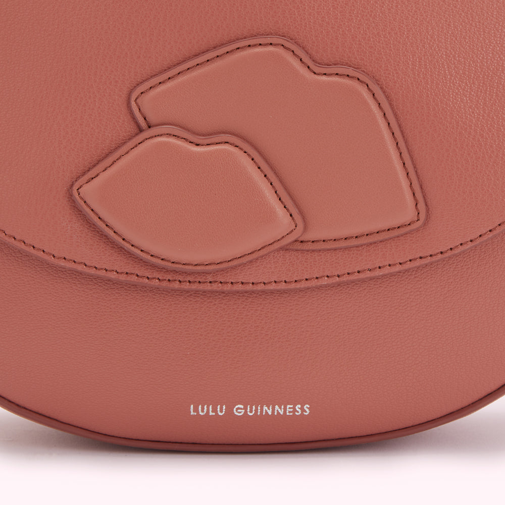 Close-up of a dusty rose Lulu Guinness handbag with embossed lips detail.
