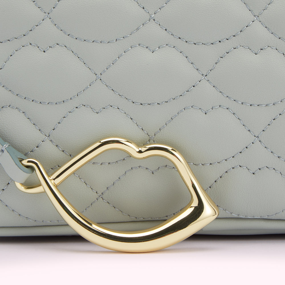 Close-up of a light teal quilted handbag with a gold lip-shaped clasp.
