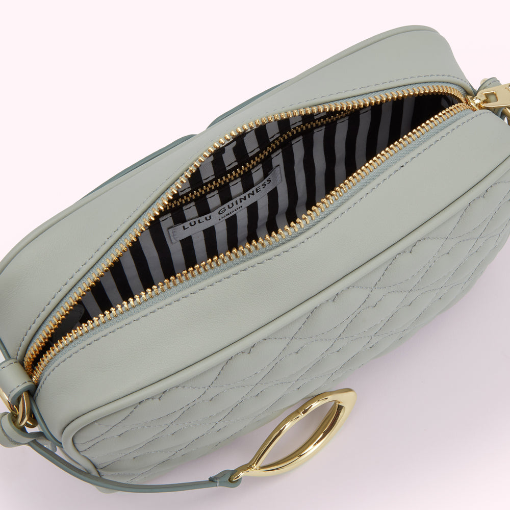 Sage green quilted Lulu Guinness crossbody bag with gold clasp open, showcasing black and white striped interior.
