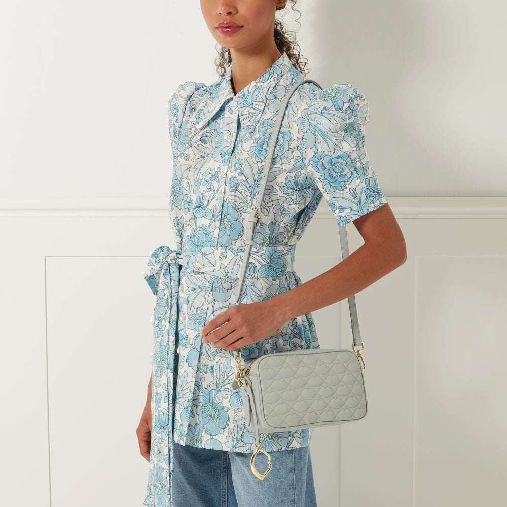 Woman in a floral dress holding a light grey quilted crossbody bag.
