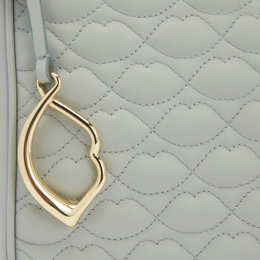 Close-up of a light grey quilted handbag with a gold lip-shaped charm.

