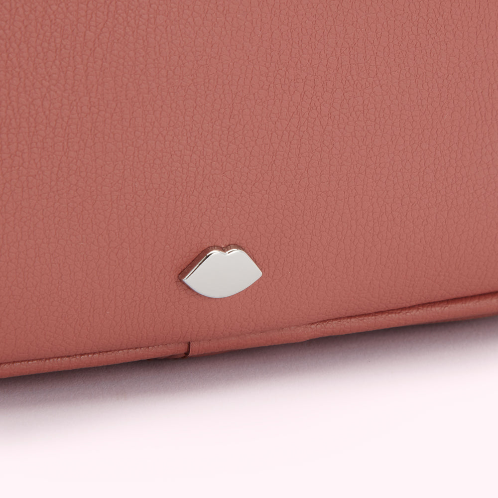 Close-up of a dusty rose-coloured purse with a silver lip-shaped emblem.
