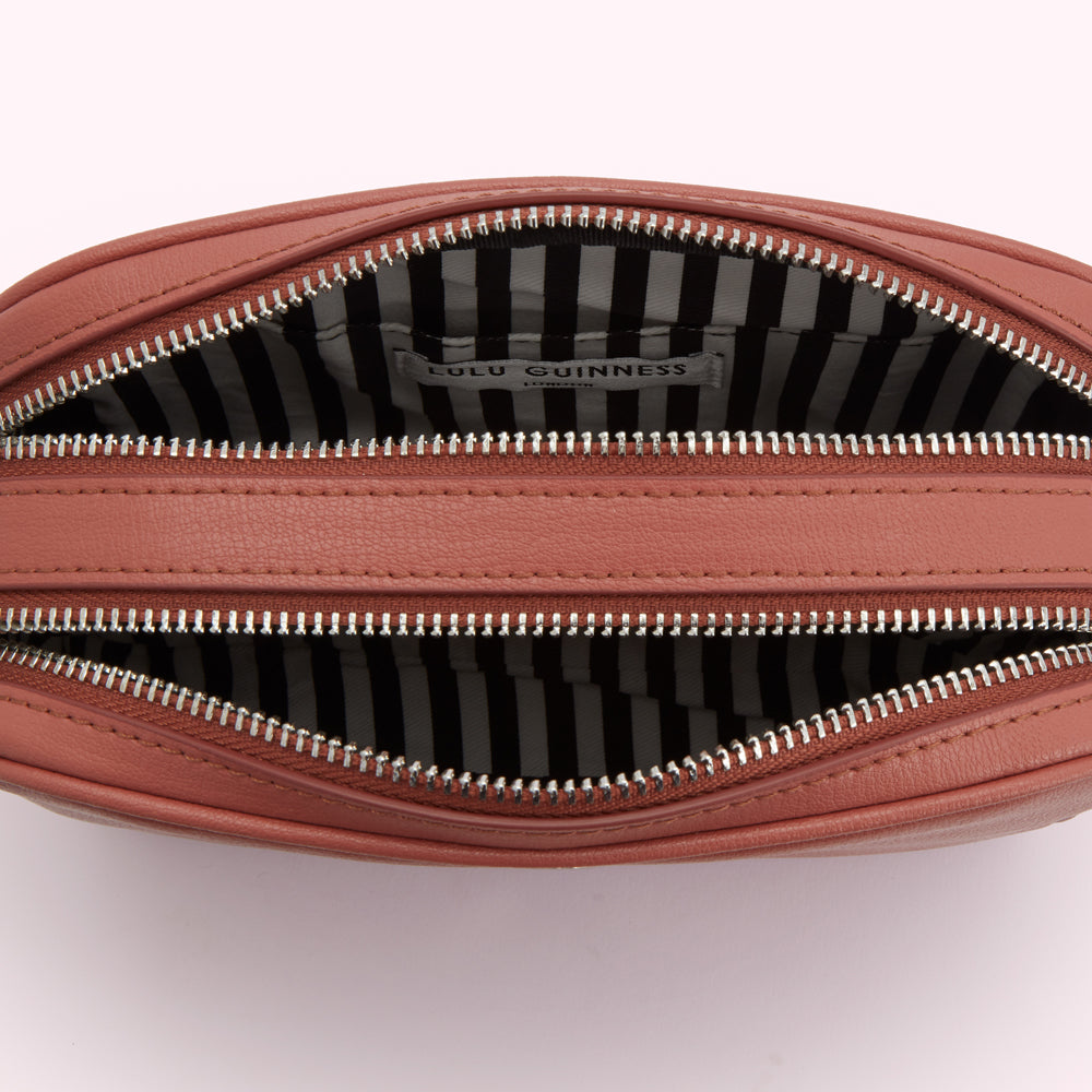 Dusty rose Lulu Guinness crossbody bag open to reveal black and white striped interior lining and brand label.