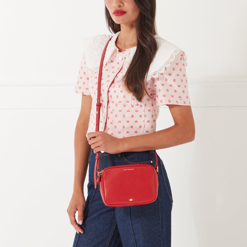 Woman with long brown hair modelling a red crossbody bag against a white background.